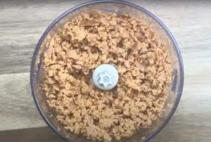 Shredded smoked turkey in a food processor bowl on a wooden surface, ready for cooking or meal prep.